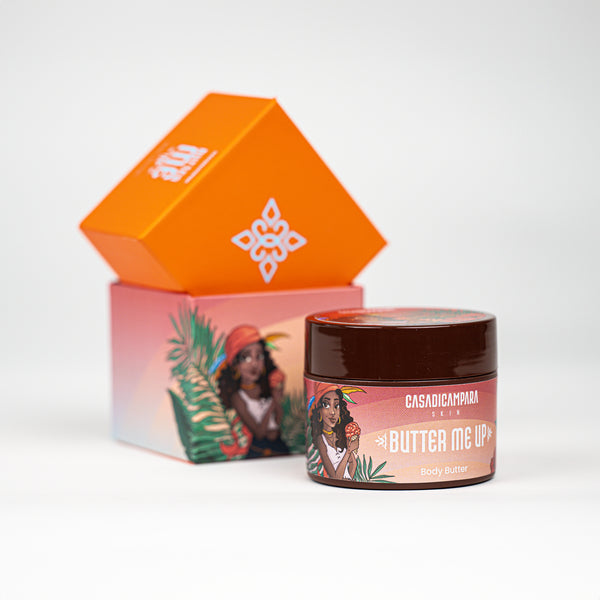 Round Butter Me Up shea body butter with girl illustration in focus and orange packaging in the background.