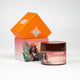 Round Butter Me Up shea body butter with girl illustration in focus and orange packaging in the background.