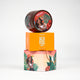 Round brown shea body butter with girl illustration placed on orange packaging with white text, body care essential.