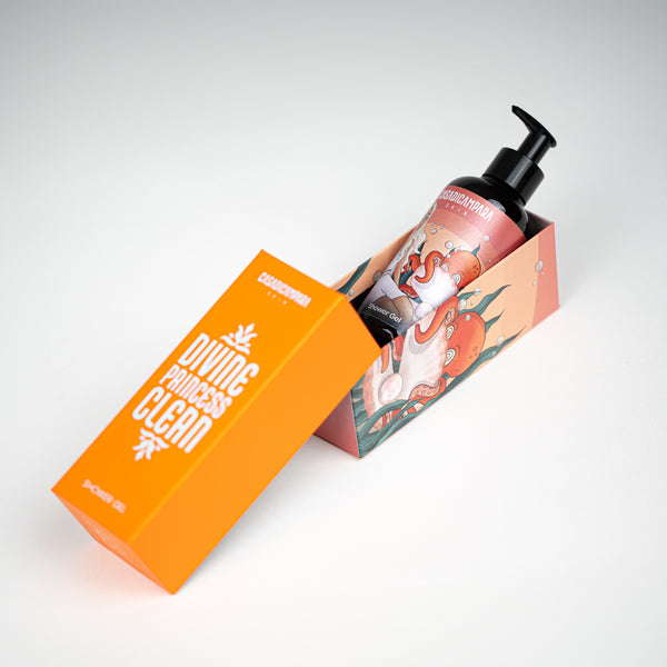 Shower gel package lying down with orange cap resting on printed bottom, featuring the bottle inside, skincare essential.