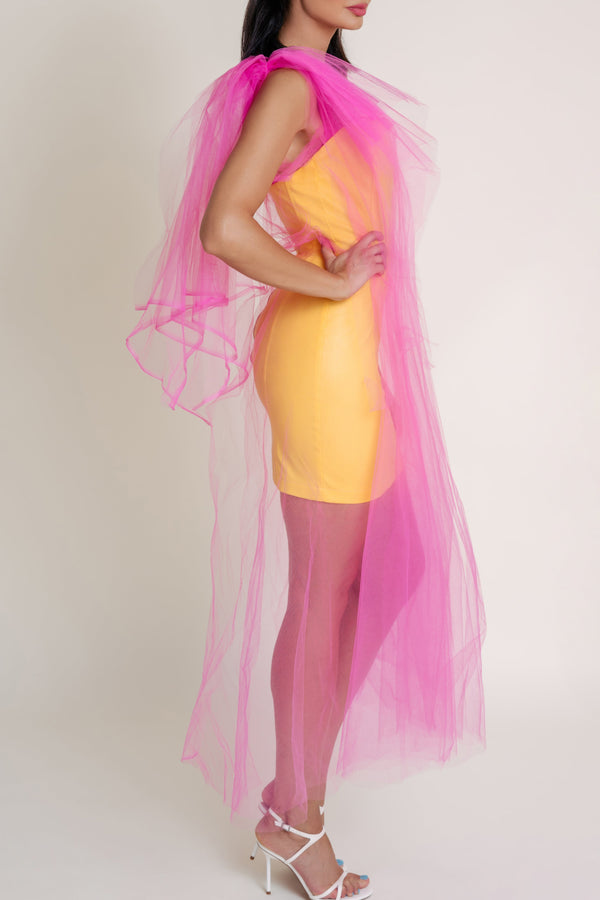 Woman standing sideways and wearing a bright yellow dress with a pink overlay against a plain background.