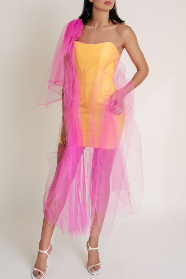 Woman is posing and wearing a yellow dress with a sheer pink overlay and white heels.