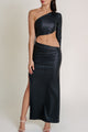 Woman in elegant black one-sleeve dress with waist cutout and high slit, paired with white high-heeled sandals.