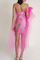Woman showing the back of a pink floral dress with a sheer overlay on a white background.
