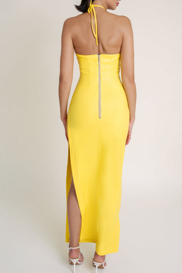 Woman wearing a yellow halter neck dress with a slit on a white background.