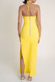 Woman wearing a yellow halter neck dress with a slit on a white background.