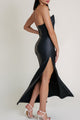 Side view of the black satin dress with high slit and open back, worn by model in soft lighting.