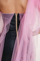 Back view of a strapless black textured dress with gold zipper, adorned with sheer pink tulle overlay for a soft, elegant touch.