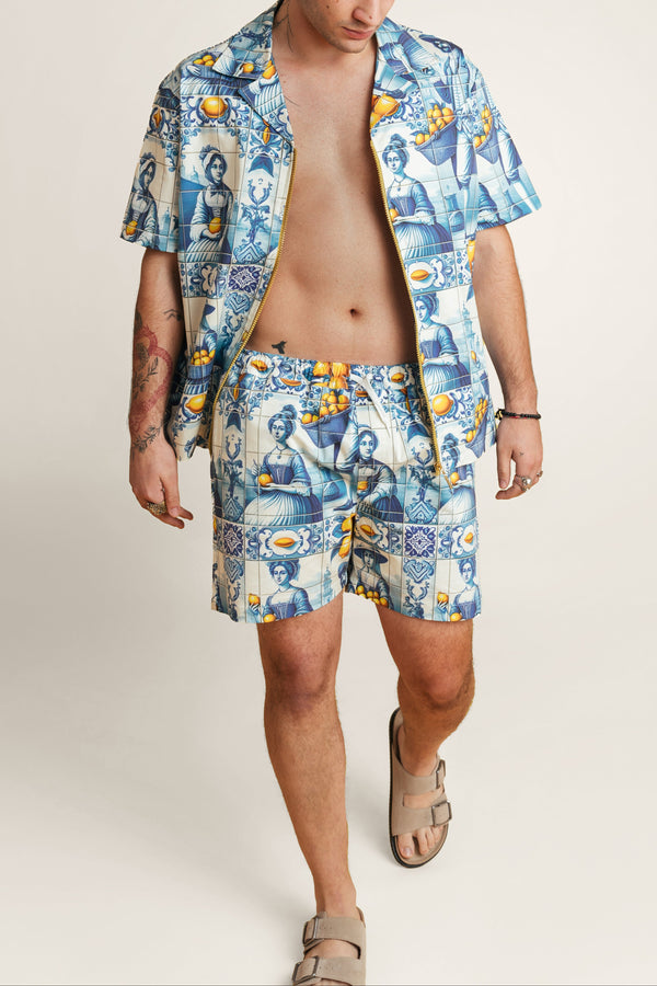 Man wearing a blue patterned shirt matching with Algarve Coast shorts on a plain background.