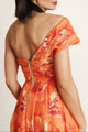 Detailed view of the orange fabric and golden zipper on a one-shoulder dress.