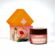 Round body scrub with orange lid in focus, beachwear girl illustration in background, summer skincare essential.